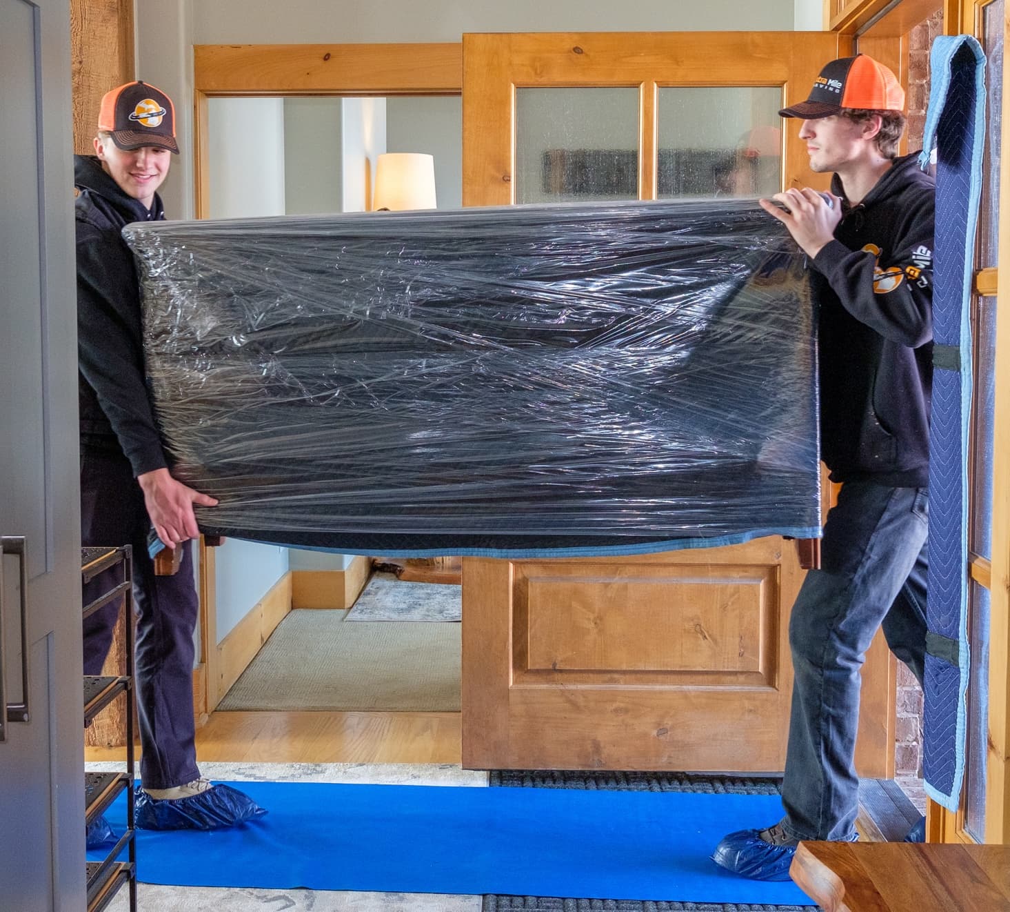 Two movers carrying a fully padded and wrapped dresser